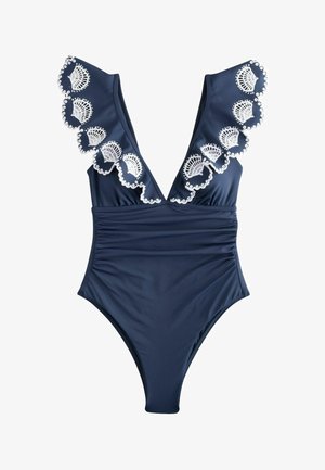 Tmavomodré jednodielne plavky s hlbokým výstrihom do V, riaseným pásom a bielou krajkou so zvlneným vzorom pozdĺž ramenných popruhov.