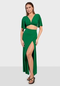 Set verde a due pezzi composto da un top corto con maniche a sbuffo e una maxi gonna con spacco alto. Realizzato in tessuto morbido e elasticizzato.