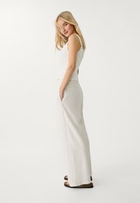 Vit ärmlös topp i kombination med vida, ljusa byxor. Outfiten har en enkel design och avslappnad passform, kompletterad med bruna sandaler.