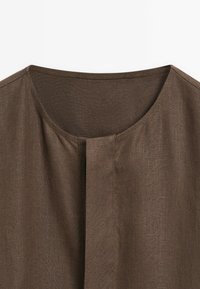 Un tissu marron texturé présente un col rond et une ouverture frontale avec de petits plis, suggérant un vêtement ample.