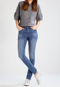 Pull gris court avec manches bouffantes, associé à un jean skinny bleu clair et des baskets argentées. Design simple avec un contraste de couleurs distinct.