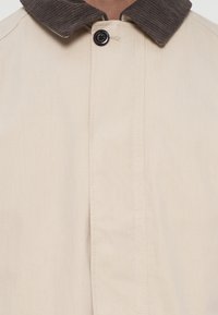 Μπεζ σακάκι με κοτλέ γιακά, με κλείσιμο με κουμπί και ευθεία ραφή. Το ύφασμα φαίνεται απαλό και ελαφρύ.