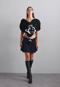 Melna oversized blūze ar balto grafisko dizainu, kombinēta ar džinsa mini svārkiem un melniem ceļa augstuma zābakiem, izceļot mūsdienīgu siluetu.