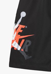 Svarta shorts med en framträdande flerfärgad grafik med "AIR" i fet stil, samt Jumpman-siluett i grå och orange accenter.