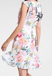 Robe blanche avec des manches froncées, ornée d'un motif floral dans des teintes de rose, vert et bleu. Tissu léger avec un ourlet évasé.