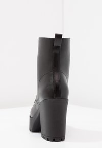 Bota negra hasta el tobillo, confeccionada en cuero suave, con un tacón cuadrado, punta redonda y una lengüeta trasera para facilitar su puesta. Suela texturizada.