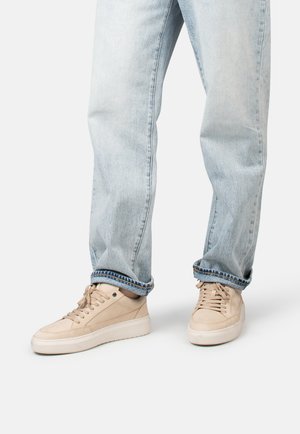 Beige Turnschuhe mit einem glatten Obermaterial aus Wildleder und Leder, runder Zehenpartie und flachen Schnürsenkeln, kombiniert mit hellblauen Jeans in entspannter Passform.