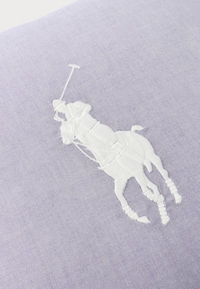 Λευκός κεντημένος παίκτης πόλο επάνω σε άλογο που κρατάει ένα μαλέτι, κεντημένος σε υφή γαλάζιου υφάσματος.