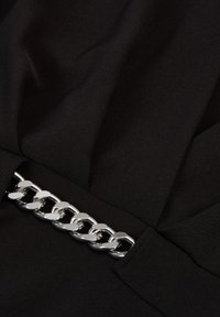 Svart tyg med en slät textur har en framträdande silverkedj-detalj vid midjan, vilket ger en metallisk accent till designen.