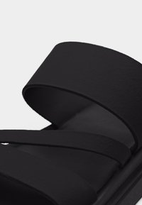 Sandale noire avec semelle large et plate, dotée de deux larges brides traversant le pied pour un ajustement sûr et un confort optimal.