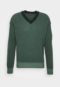 Pull vert tricoté avec un col en V, tissu texturé, col noir contrastant, poignets et ourlet côtelés. Pas de motifs ni de logos visibles.