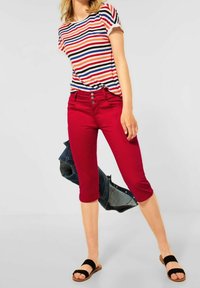 Pantalones cortos rojos combinados con una blusa de mangas cortas a rayas. La blusa presenta rayas horizontales en rojo, azul y negro. Sandalias negras.