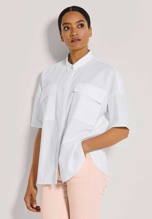 Witte korte mouwen blouse met een kraag, twee borstzakken, een relaxte pasvorm en zijsplitten, gedragen met lichtroze broeken.
