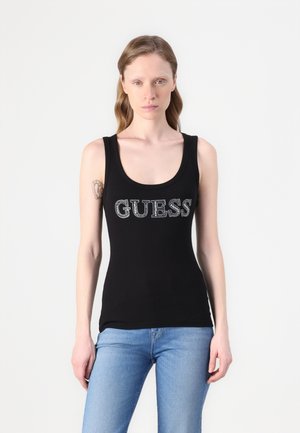 Canotta nera in cotone con scollo a barca. Presenta un logo argento "GUESS" sulla parte anteriore. Abbinata a jeans azzurri chiari.