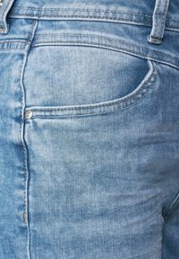 Faded blue denim jeans featuring a back pocket with a metal snap. The fabric texture is soft with subtle variations in color.