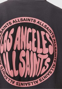 Czarna koszulka z dużym różowym graficznym napisem w kształcie okręgu, który brzmi "LOS ANGELES ALLSAINTS". Materiał wydaje się miękki, a krój jest standardowy.