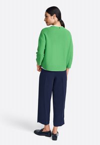 Groen gestructureerd sweater met driekwart mouwen, gecombineerd met marineblauwe wijde broek en donkere instappers; eenvoudig ontwerp en effen kleuren.