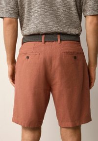 Lette, rustfarvede linnedshorts med lige pasform, der har to baglommer og et bælte med sort-hvide mønstre.