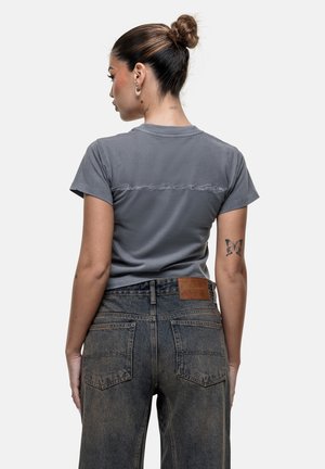 Grijze slim-fit t-shirt met korte mouwen, voorzien van een subtiele scriptontwerp op de rug. Gecombineerd met hoge taille, vervaagde blauwe jeans.