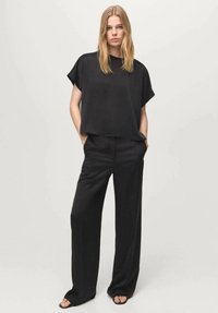 Schwarzes Kurzarmoberteil kombiniert mit weiten, locker sitzenden schwarzen Hosen. Beide Kleidungsstücke zeichnen sich durch eine glatte Textur und minimalistisches Design aus.