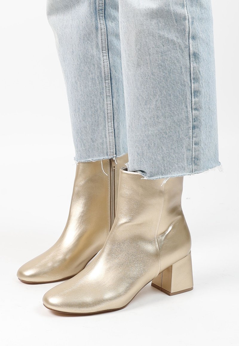 Bottes beige brillantes à talons carrés portées avec un jean court bleu clair aux ourlets effilochés sur fond blanc.