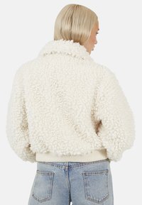 Witte, donzige, korte jas met een zachte, gestructureerde buitenkant, brede kraag en geribde zoom. Gecombineerd met licht gewassen jeans.