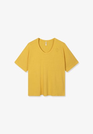 Camiseta amarilla de manga corta con cuello redondo y pequeño detalle en relieve de un personaje en la parte superior izquierda del pecho sobre fondo blanco.