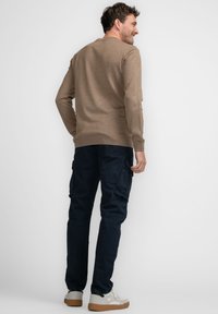 Bruine gebreide trui met een ronde hals, gecombineerd met donkerblauwe cargobroek met zakken, en witte sneakers met een rubberen zool.