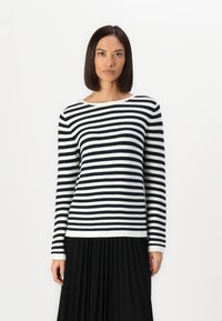 Gestreiftes Schwarz-Weiß-Pullover mit Rundhalsausschnitt, langen Ärmeln und gerippter Textur, kombiniert mit einem plissierten schwarzen Rock.