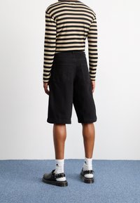 Černé bavlněné kraťasy s volným střihem, bočními kapsami a ohrnutým lemem. Spárovány s pruhovanou košilí s dlouhým rukávem a černou obuví.