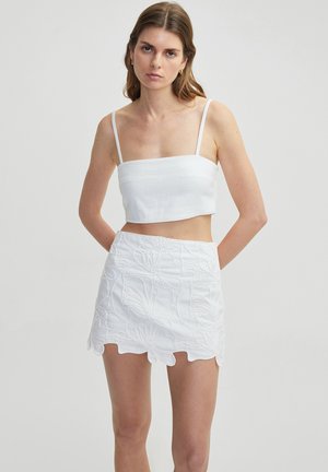 White crop top with thin straps, featuring a textured fabric. White mini skirt with floral embroidery and scalloped hemline.