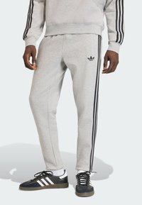 Sivé teplákové nohavice s čiernymi bočnými pruhmi a nenápadným logom na ľavom stehne. Vyrobené z jemnej tkaniny s zúženým strihom.