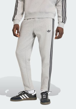 Sivé teplákové nohavice s čiernymi bočnými pruhmi a nenápadným logom na ľavom stehne. Vyrobené z jemnej tkaniny s zúženým strihom.