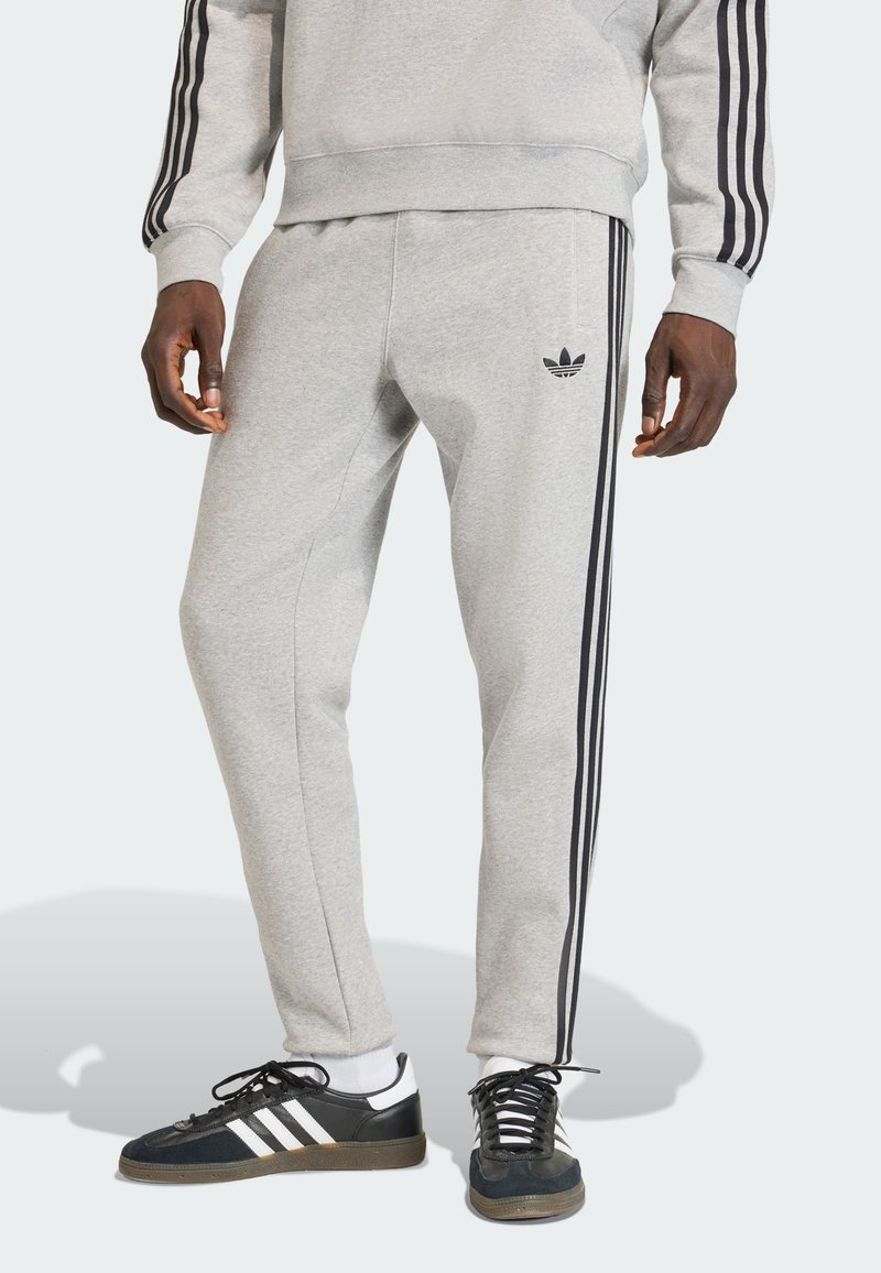 Sivé teplákové nohavice s čiernymi bočnými pruhmi a nenápadným logom na ľavom stehne. Vyrobené z jemnej tkaniny s zúženým strihom.