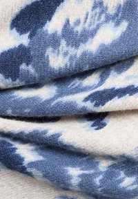 Strickstoff mit cremefarbenem Grund und blauen sowie marineblauen abstrakten Mustern, glatter Textur und einem weichen, warmen Aussehen.