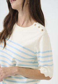 Pull crème à manches courtes avec des rayures bleu clair et blanches ; présente des boutons décoratifs à l'épaule et un ourlet festonné.