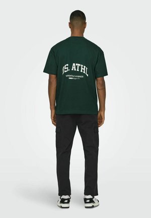 Groene katoenen t-shirt met witte bedrukte tekst op de achterkant, gecombineerd met zwarte cargobroek. Heeft een relaxte pasvorm en korte mouwen.