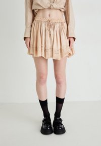 Peach fabric skirt with a flared design, gathered waistband, and raw hem. Paired with black socks and chunky black shoes.