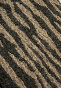 Beige textiel met een zwart gestreept patroon, met een gladde textuur en een geweven afwerking. Randen vertonen lichte rafeling.