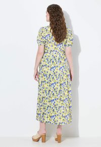 Květinové maxi šaty v žlutých, modrých a zelených tónech. Rukávy ve stylu puff, obepnutý vršek a splývavá sukně s rozparkem vzadu. Nosené s béžovými platformovými podpatky.