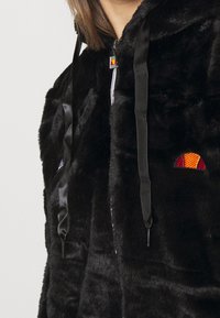 Felpa nera in pile con zip, dotata di lacci in raso, e un piccolo logo semicircolare arancione e rosso sul petto.