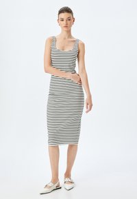 Zwart-witte gestreepte midi-jurk met een vierkante halslijn en brede banden, gemaakt van een gladde, elastische stof. Draagt een paar puntige witte flats.