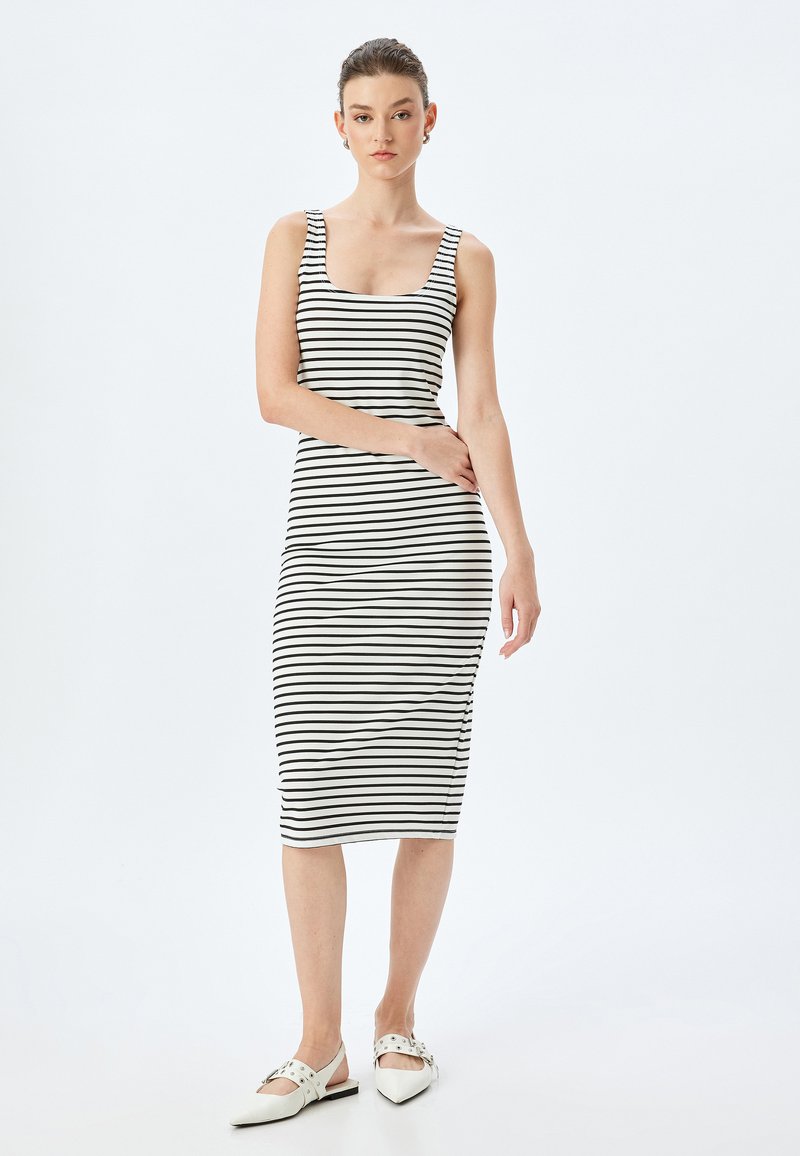 Zwart-witte gestreepte midi-jurk met een vierkante halslijn en brede banden, gemaakt van een gladde, elastische stof. Draagt een paar puntige witte flats.