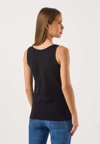 Svart ärmlös t-shirt med rund halsringning, figursydd form och slät textur; kombinerad med blåa jeans i denim.