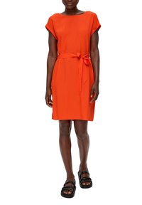 Oranje jurk met korte mouwen, een aangesloten taille en een strik aan de voorkant, gemaakt van een gladde, lichtgewicht stof. Zwarte sandalen worden apart gedragen.