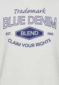 Tela blanca con texto azul que dice "Marca Registrada BLUE DENIM EST. 1993 RECLAMA TUS DERECHOS" junto a un diseño gráfico.