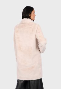 Kabát z umělé kožešiny v světle růžové barvě s měkkým a texturovaným povrchem. Má šálový límec a uvolněný střih, končí pod boky.