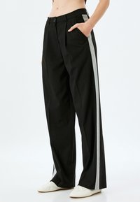 Zwarte wijde broek met een contrasterende grijze zijstribe, voorzakken, een knoopsluiting en een gladde, gestructureerde stof.