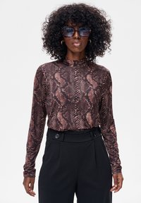 Top z długim rękawem w brązowy wzór węża, z wysokim kołnierzem. Połączony z czarnymi spodniami o wysokim stanie z ozdobnymi guzikami.