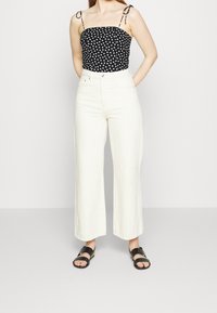 Top a pois bianco e nero con spalline sottili, abbinato a pantaloni a gamba larga bianchi a vita alta e sandali neri.